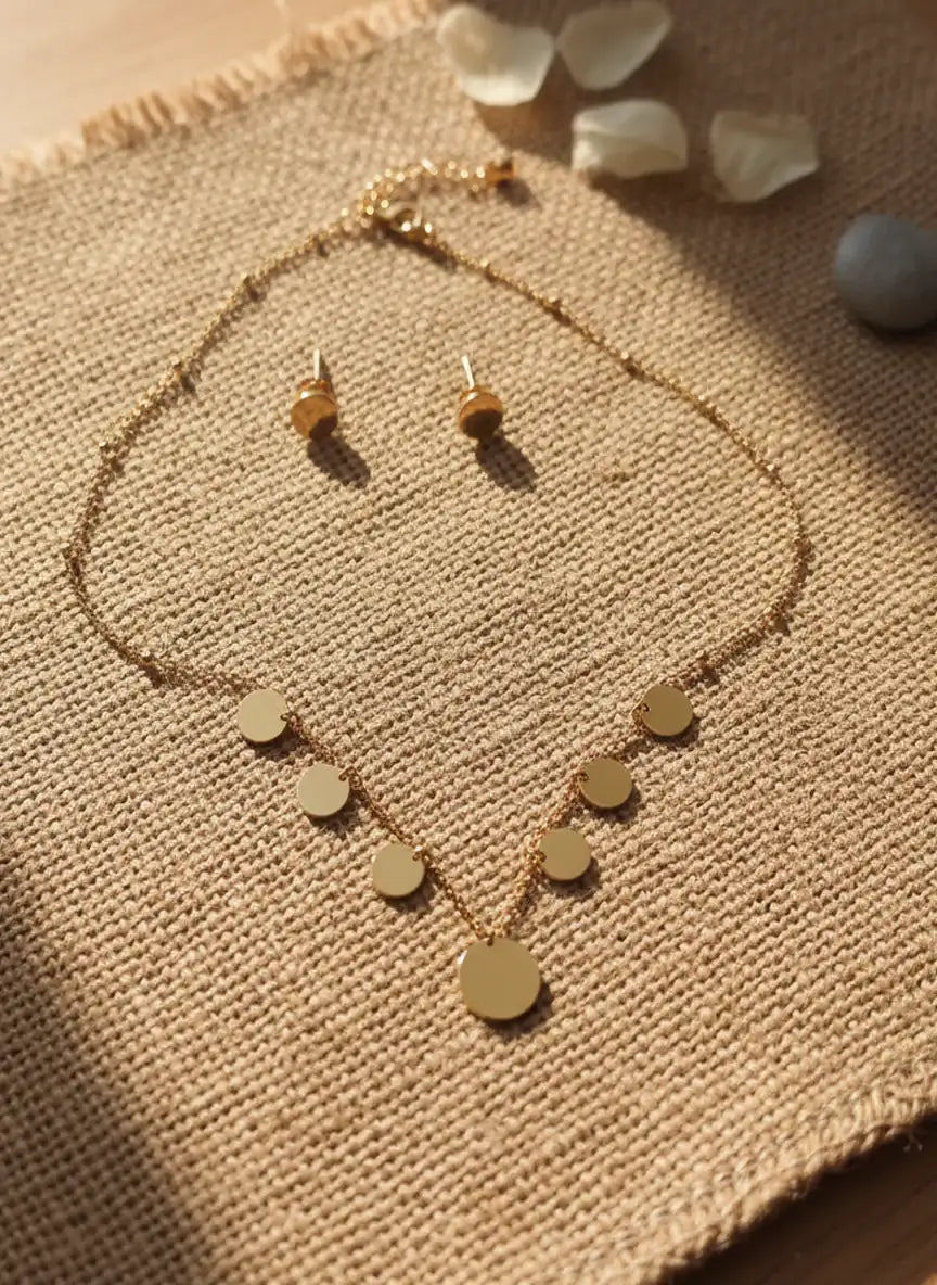 Gold necklace and earrings set on a textured fabric surface with small stones.