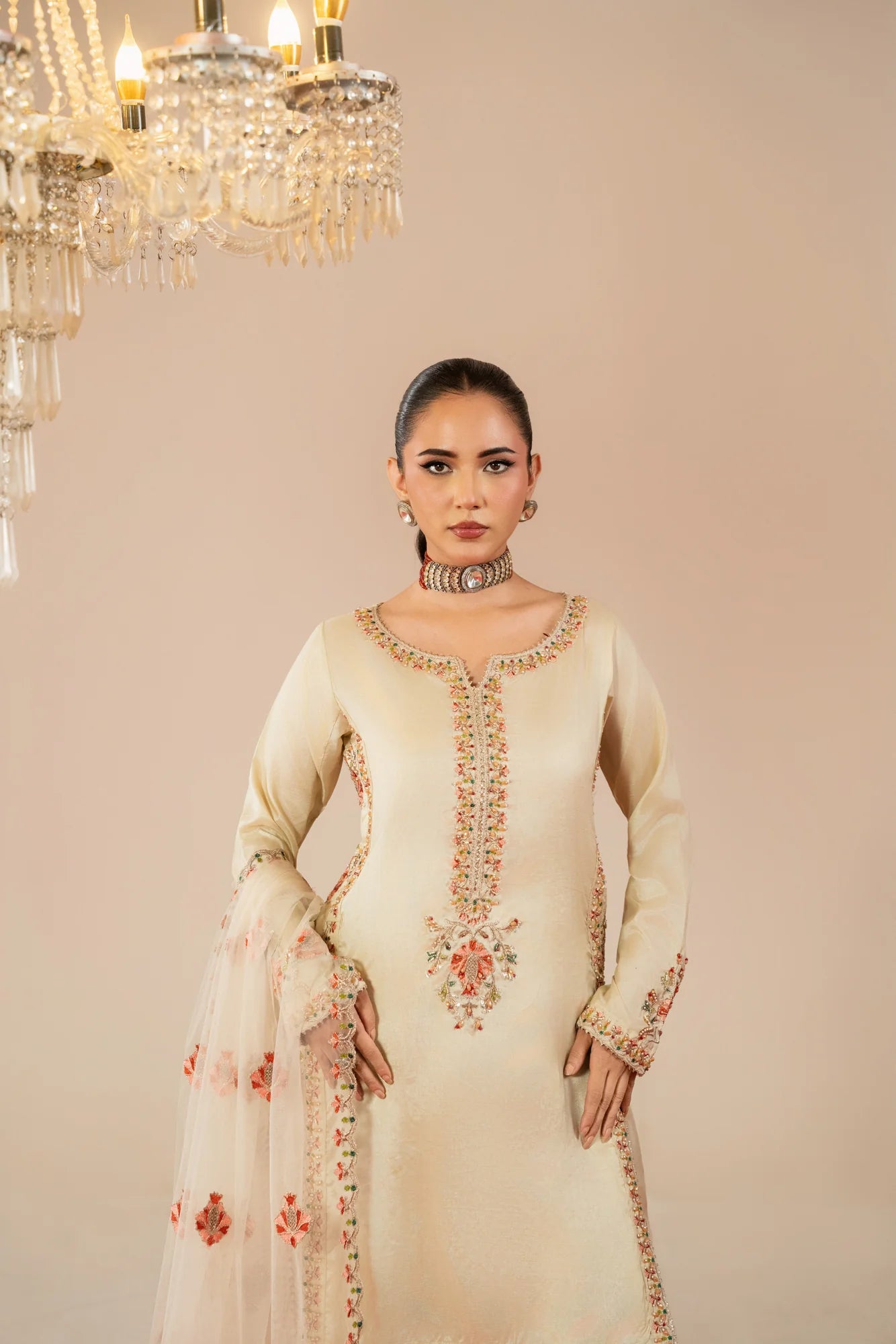 Woman in a cream embroidered outfit standing under a chandelier