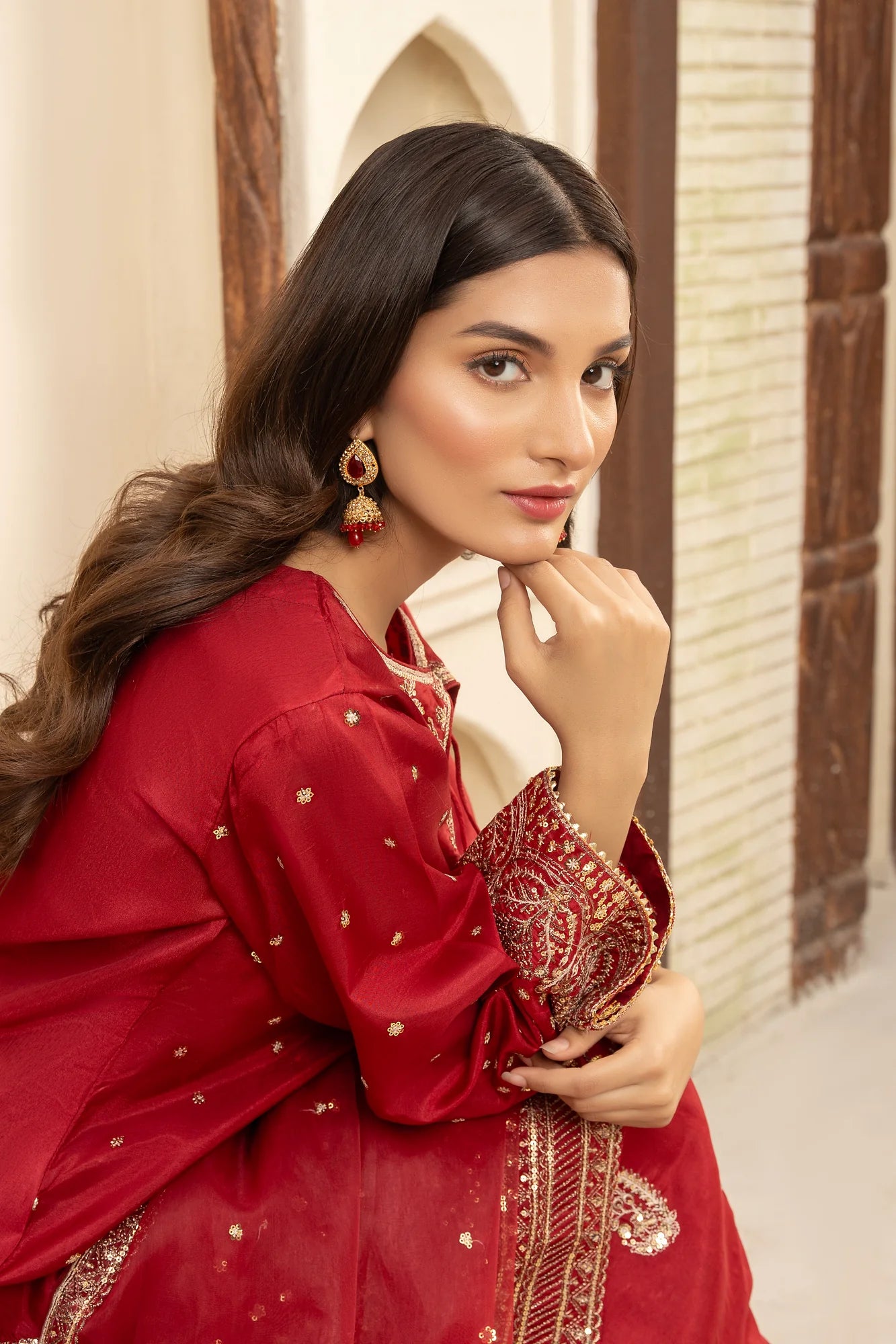 Woman in a red traditional outfit with intricate designs, posing indoors.