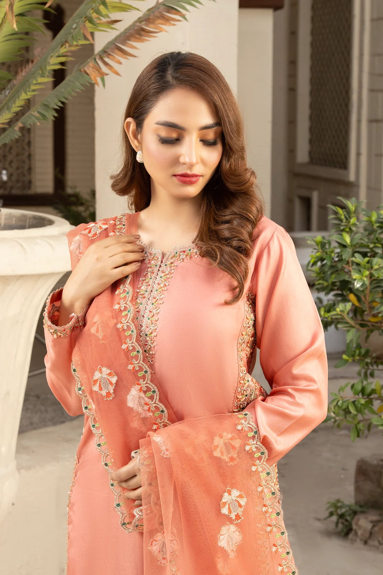 Woman wearing a peach embroidered traditional outfit outdoors.