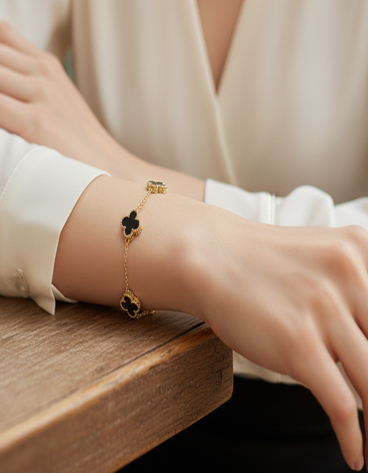 Gold bracelet with black clover charms on a person's wrist against a neutral background