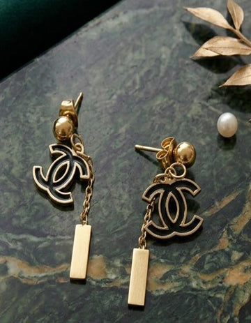 Gold earrings with CC logo on a dark surface