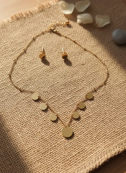 Gold necklace and earrings set on a textured fabric surface with small stones.