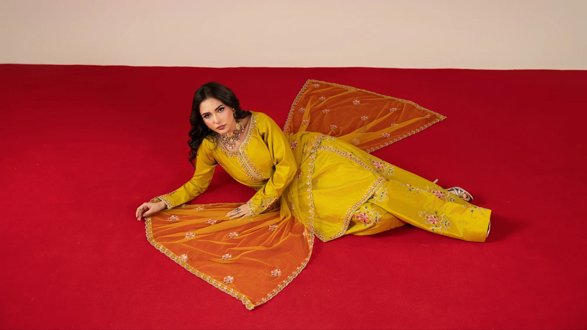 Woman in a yellow traditional outfit with an orange dupatta on a red background