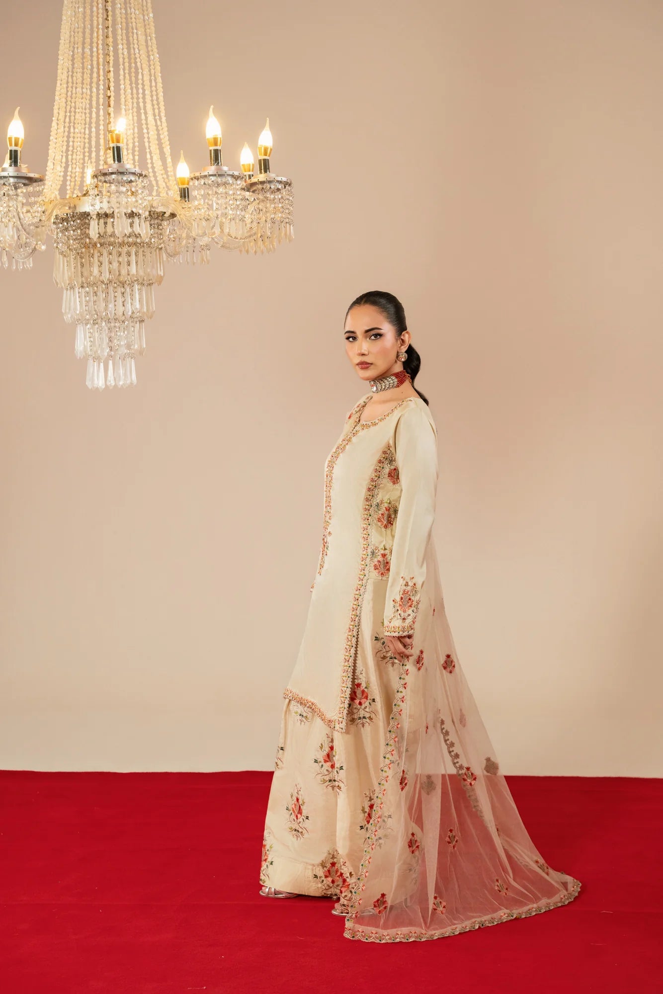Woman in a floral dress standing on a red carpet with chandeliers in the background