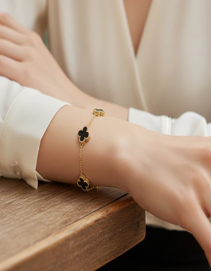 Gold bracelet with black clover designs on a wrist against a neutral background