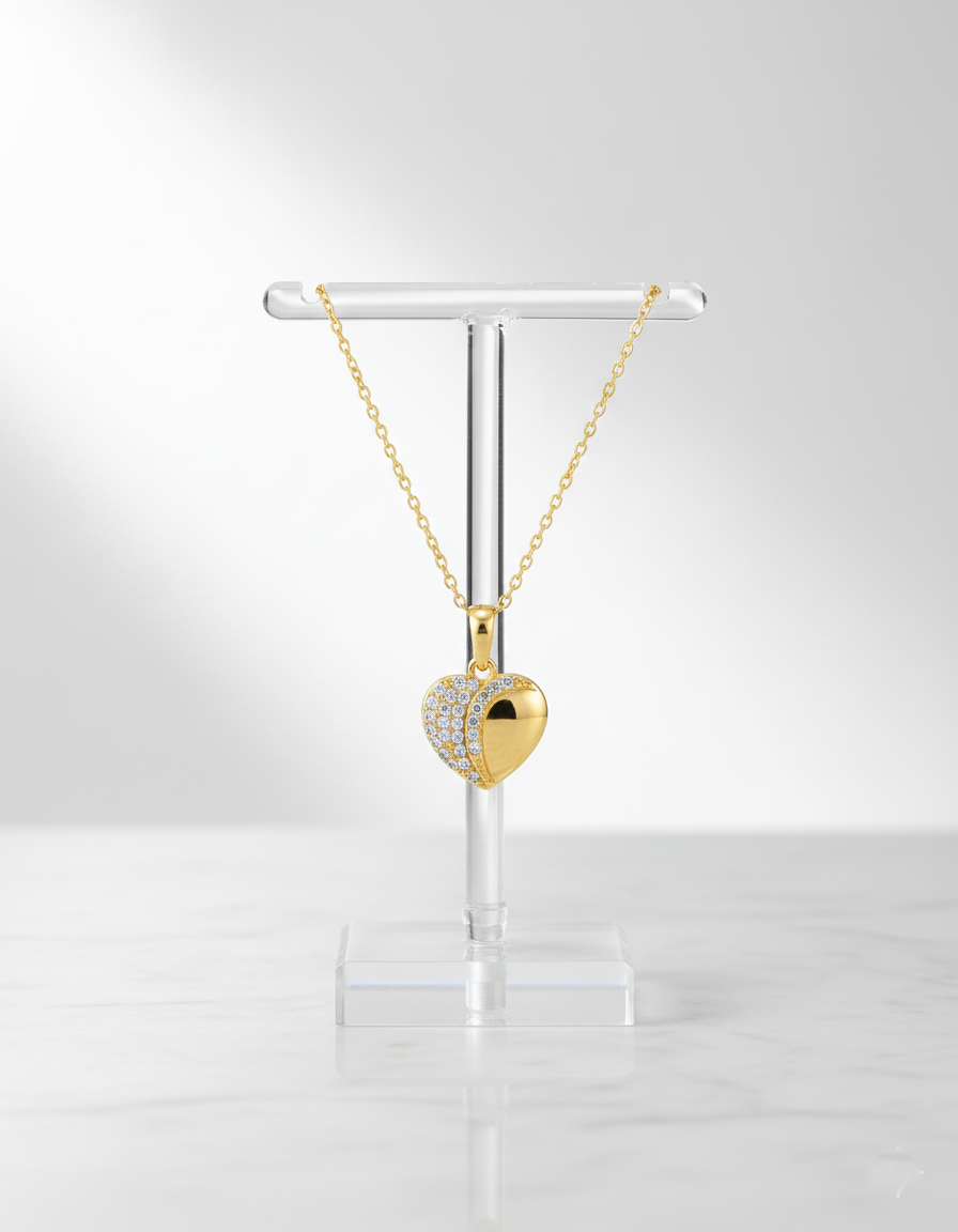 Gold heart-shaped necklace on a clear stand against a white background