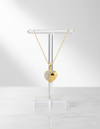 Gold heart-shaped necklace on a clear stand against a white background