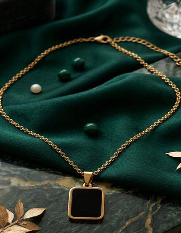 Gold necklace with a black square pendant on a green fabric background