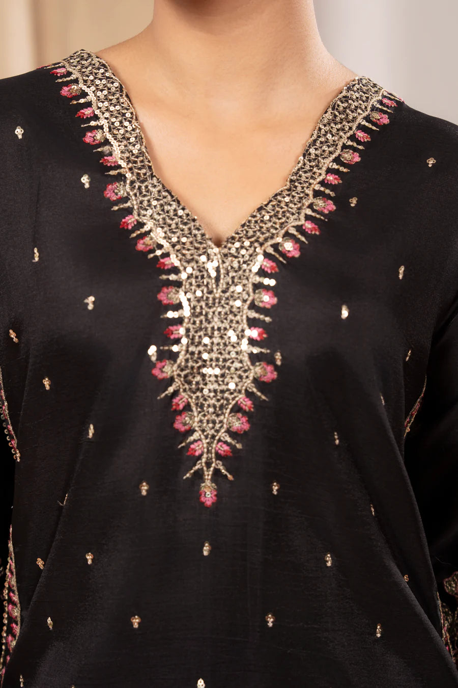 Black garment with intricate gold and pink embroidery on a neutral background