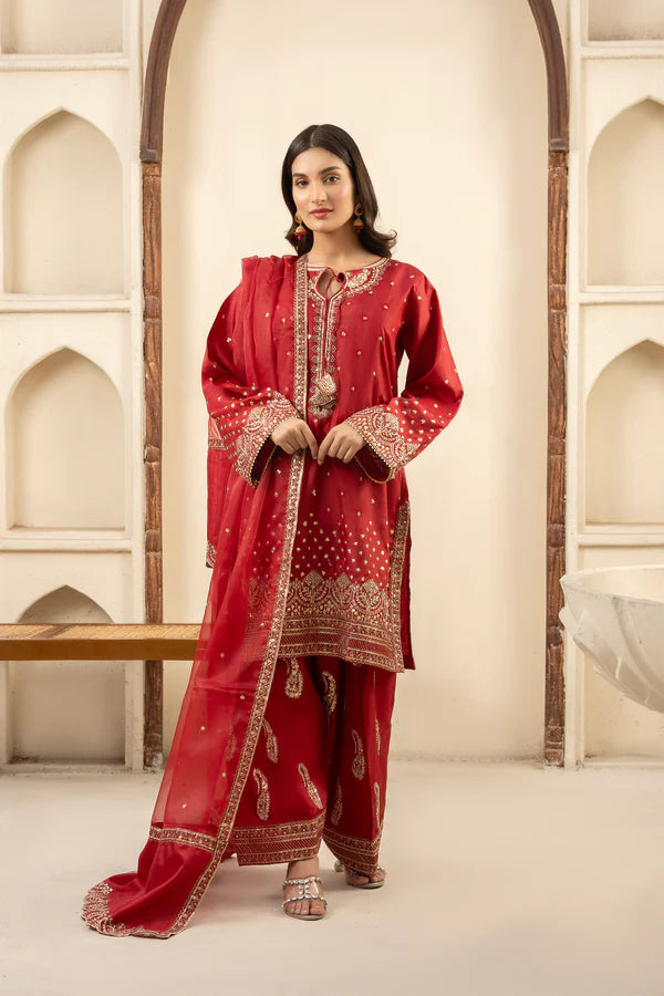 Woman wearing a red traditional outfit with intricate patterns in a decorative setting.
