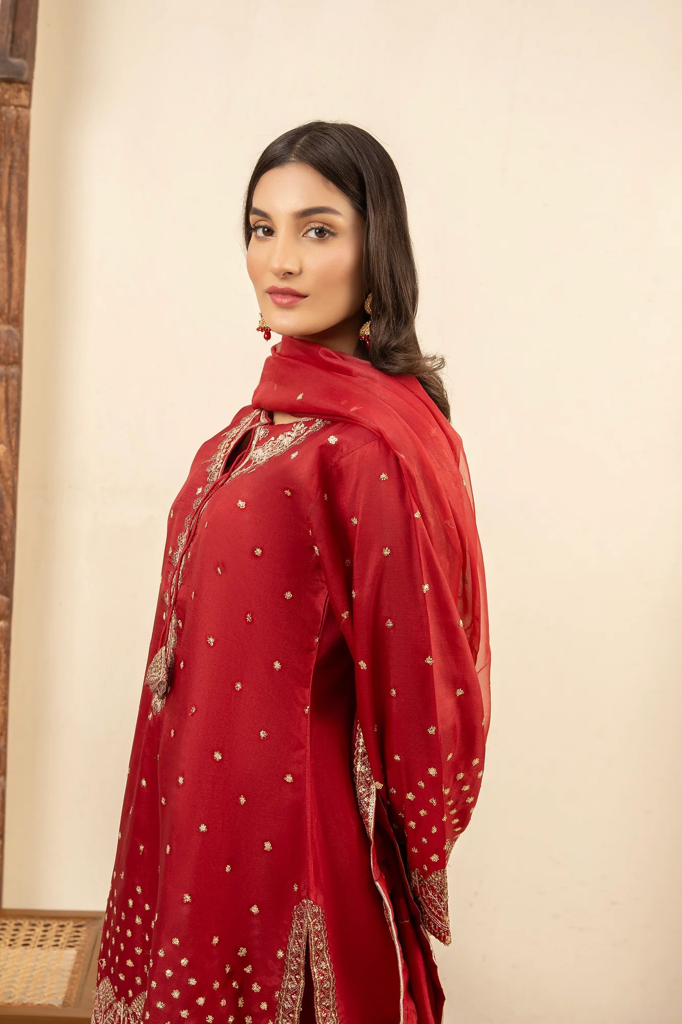 Woman wearing a red traditional outfit with intricate patterns against a neutral background