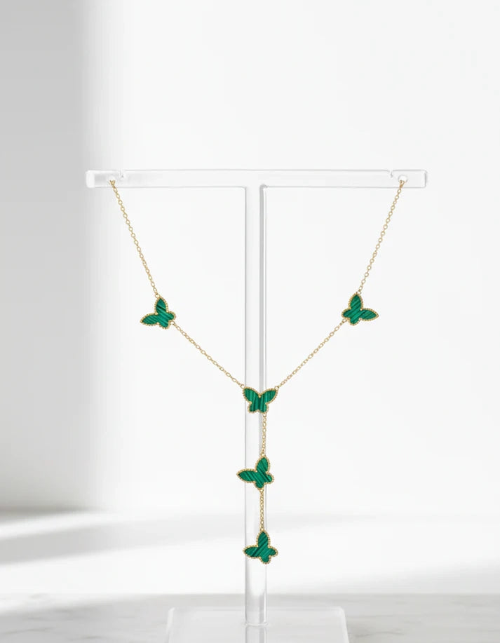 Necklace with green butterfly pendants on a clear stand against a white background