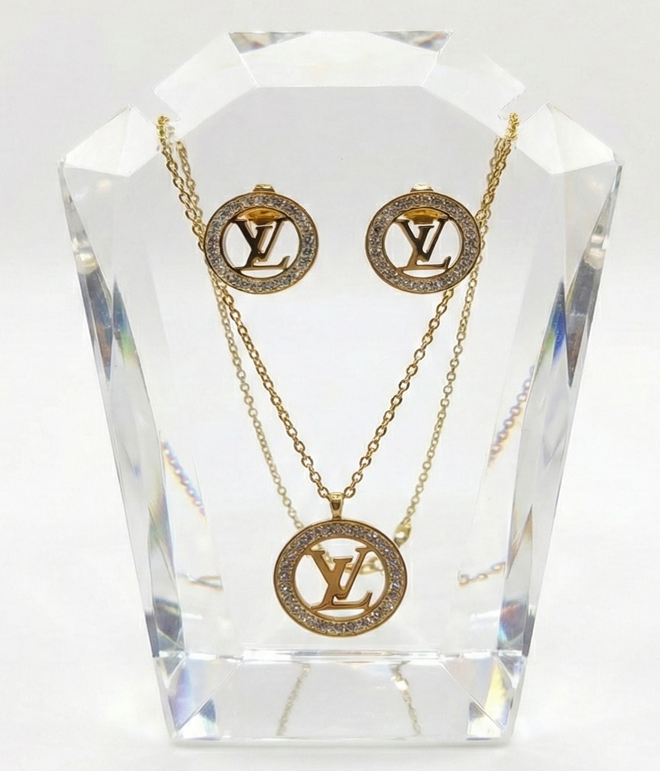 Gold necklace and earrings with Louis Vuitton logo on a crystal stand