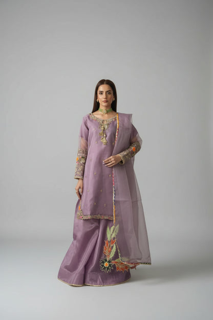 Woman in a purple traditional outfit standing in a room with decorative elements.