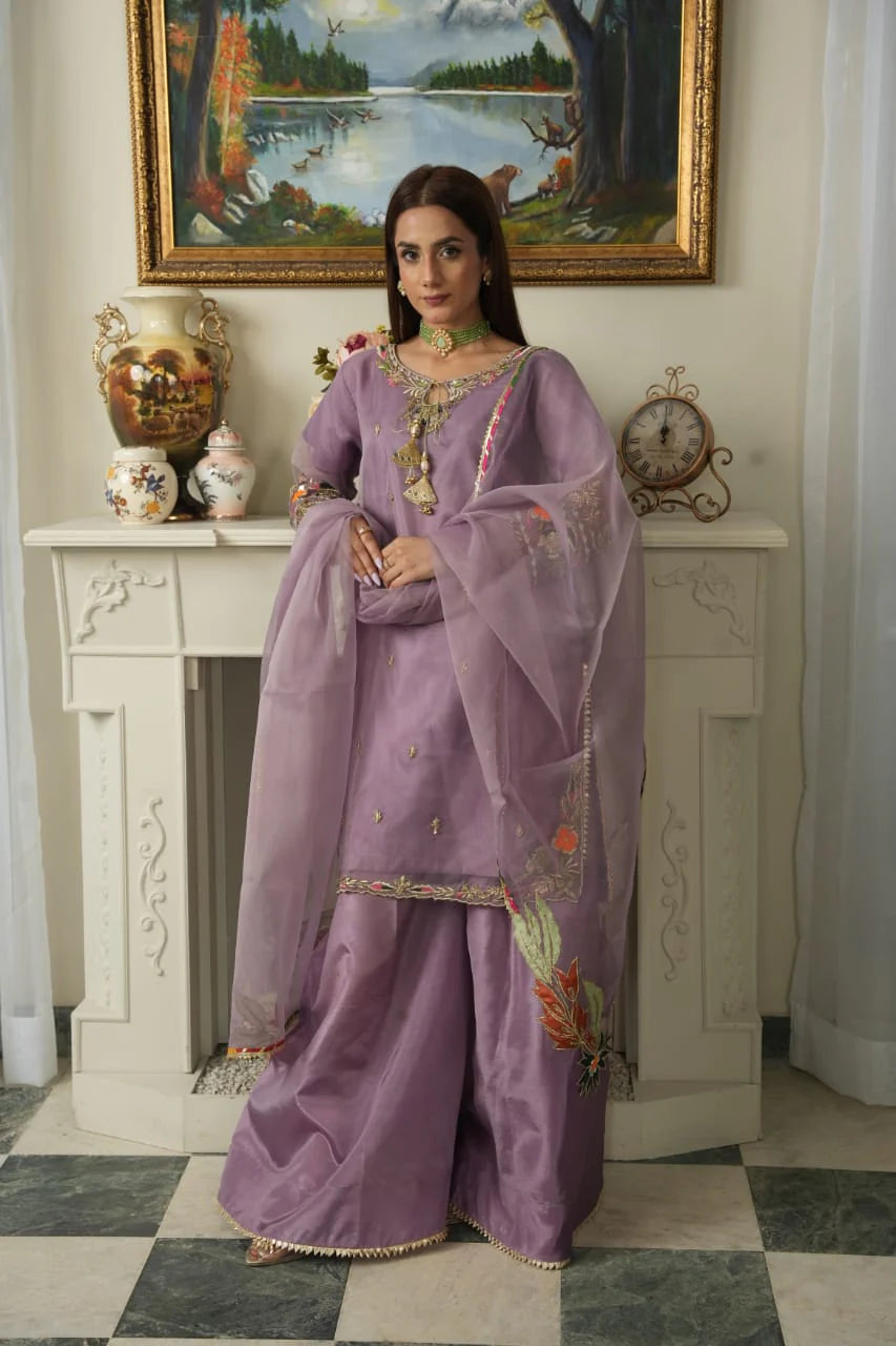 Woman in a purple traditional outfit standing in a room with a painting on the wall.