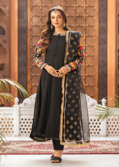 Woman in a black traditional outfit with floral patterns standing in an ornate indoor setting.