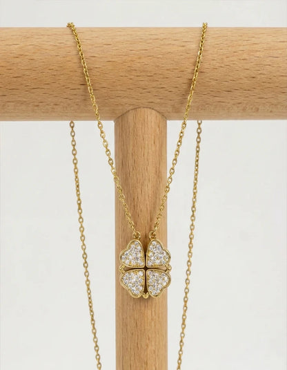 Gold necklace with a clover-shaped pendant on a wooden stand against a white background