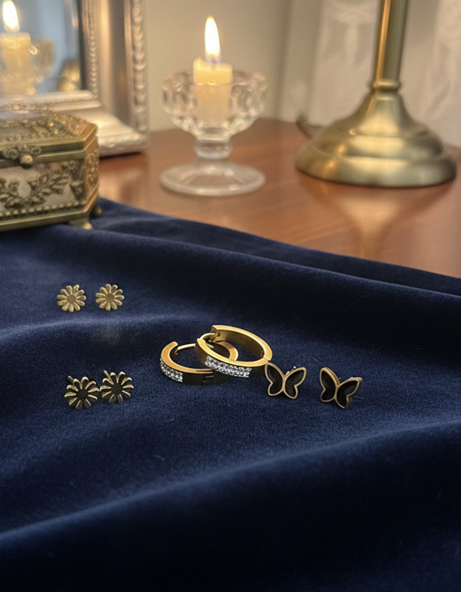 Gold jewelry including rings and earrings on a blue fabric with candles in the background