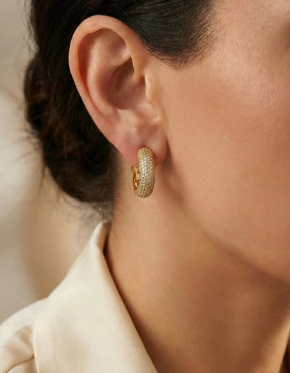 Close-up of a person wearing gold hoop earrings with a blurred background