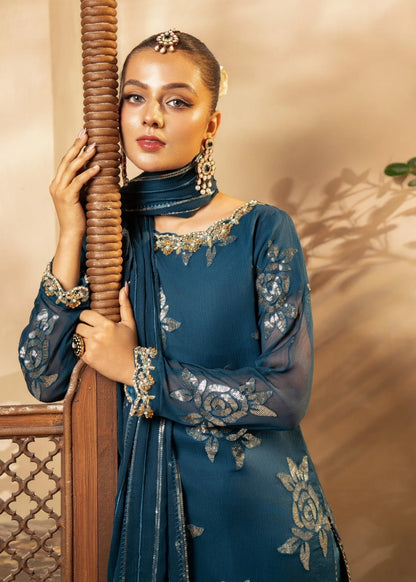 Woman in a blue traditional outfit holding a wooden rod against a beige wall.
