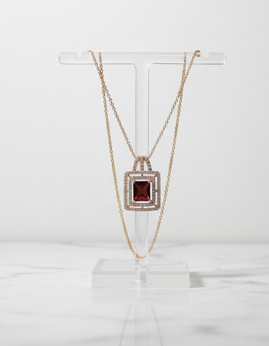 Gold necklace with a red gemstone pendant on a clear stand against a white background