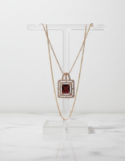 Gold necklace with a red gemstone pendant on a clear stand against a white background