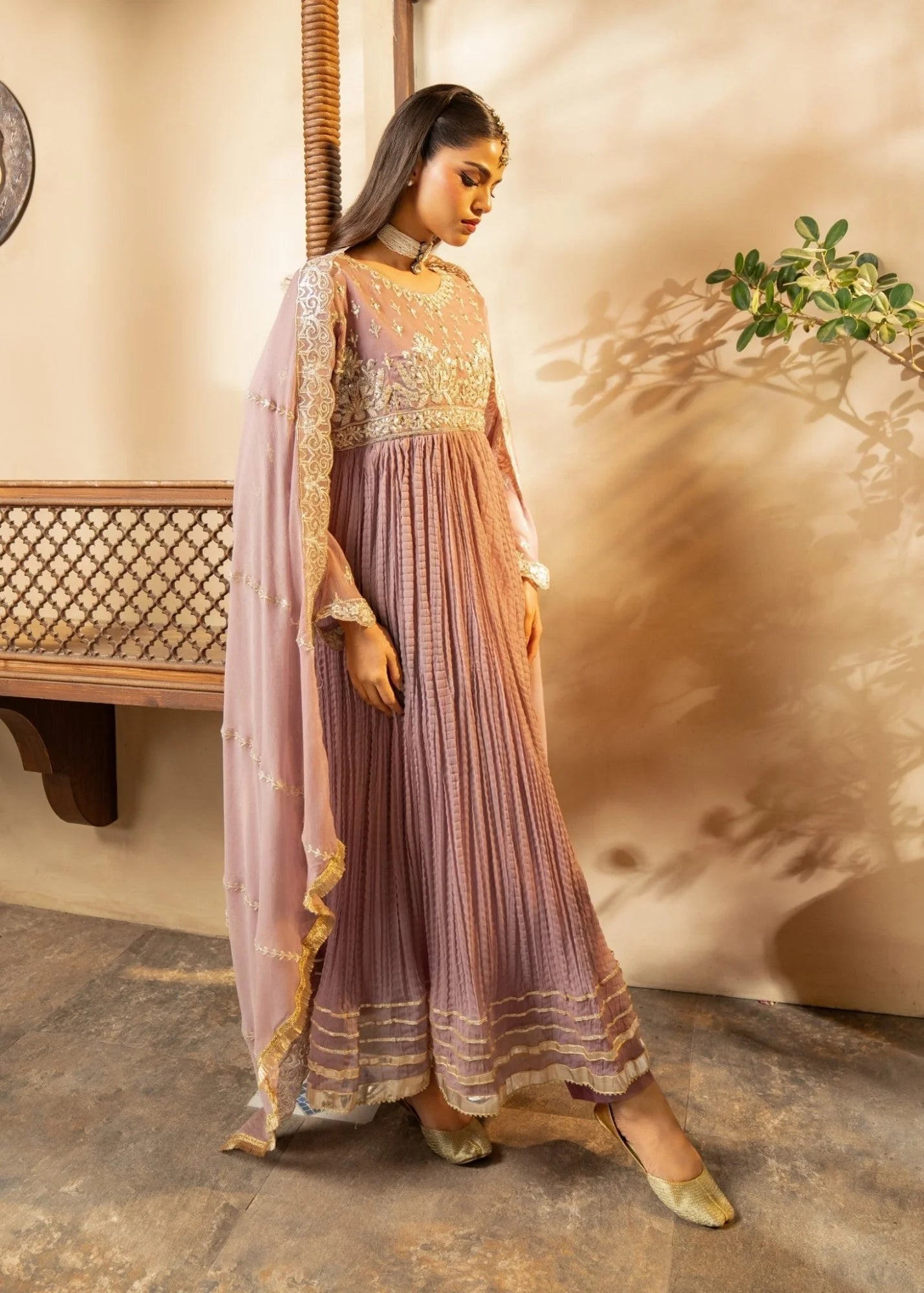 Woman in a traditional outfit with a soft pink dress and gold accents, standing indoors.