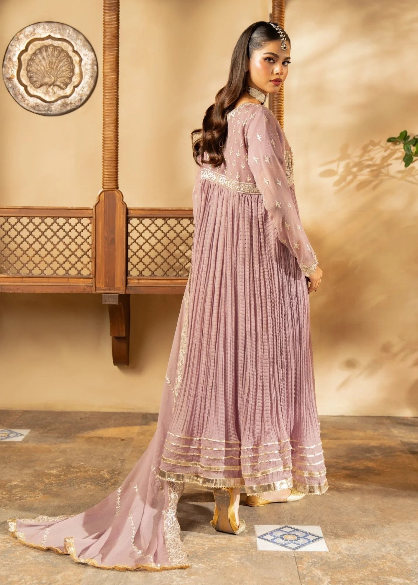 Woman in a pink traditional outfit standing in a room with a decorative wall.