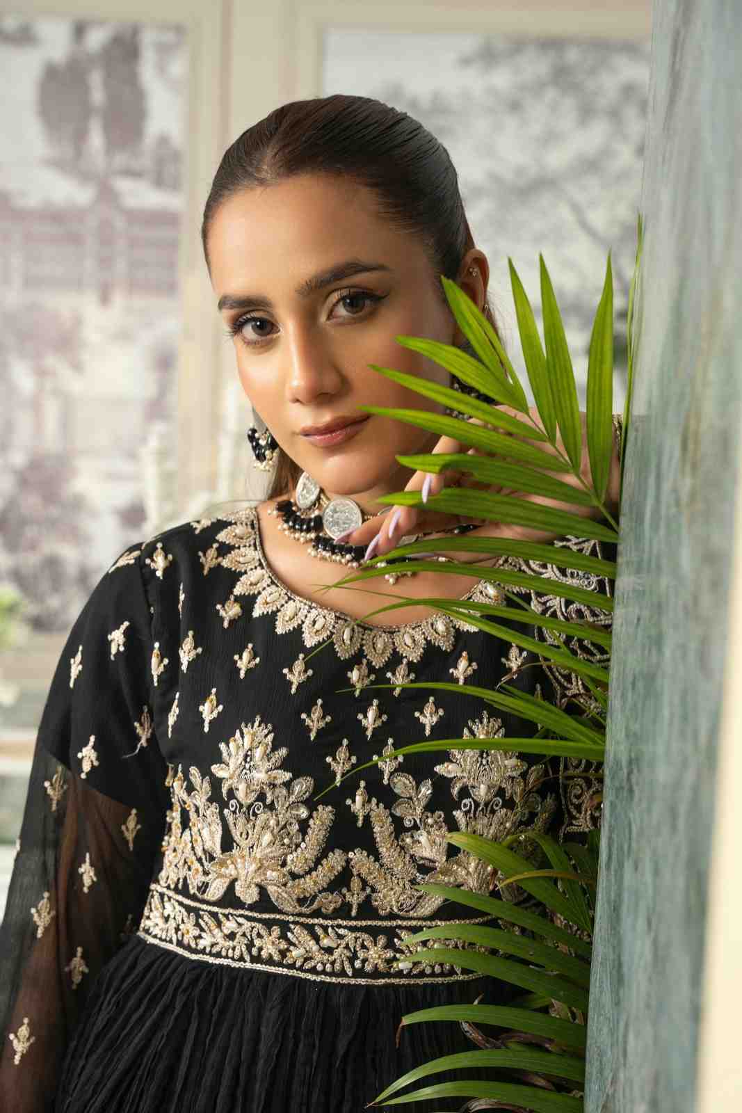 Woman wearing a black and gold embroidered outfit with a plant in the foreground