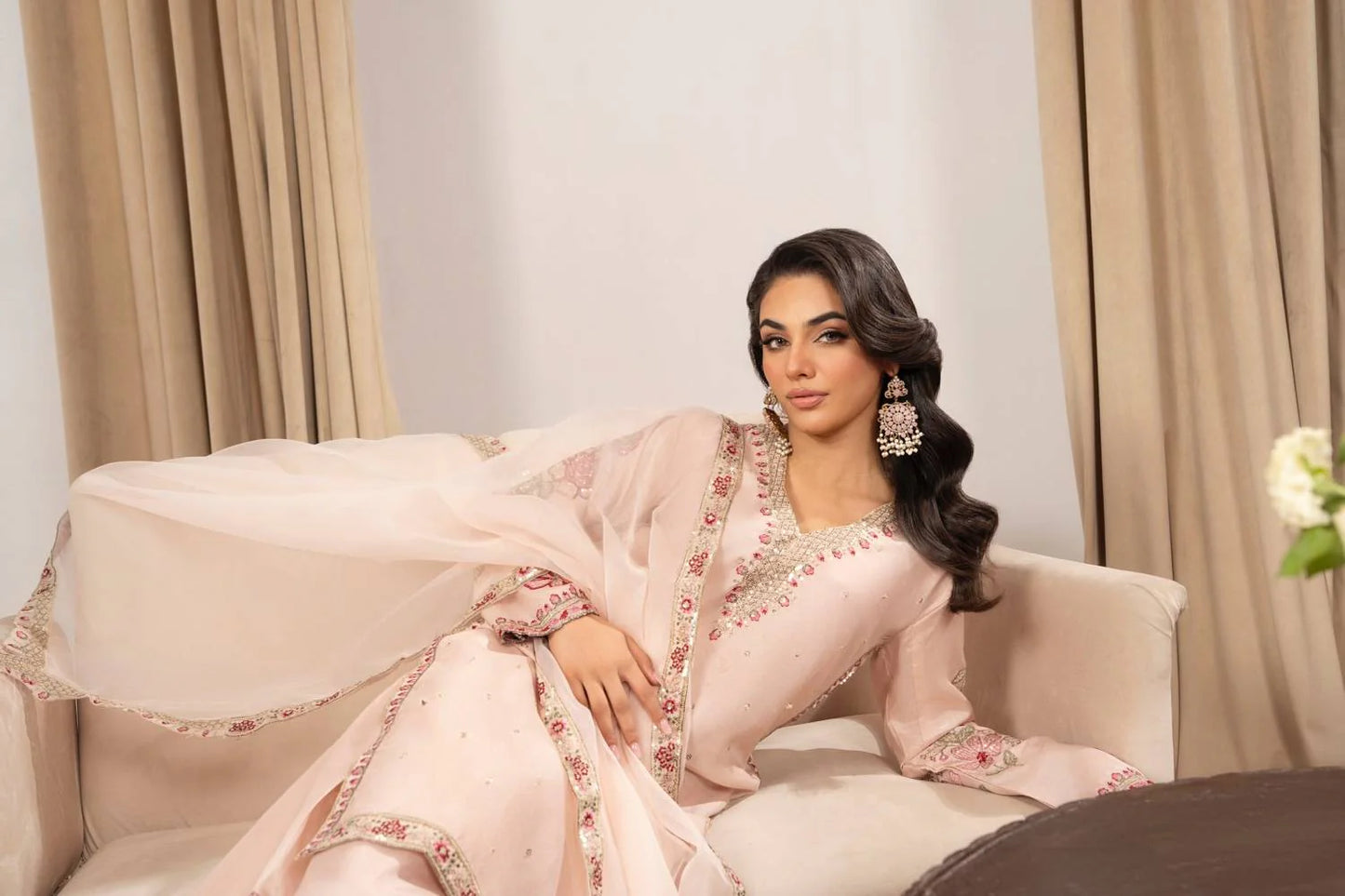 Woman in a pink traditional outfit sitting on a couch with beige curtains in the background
