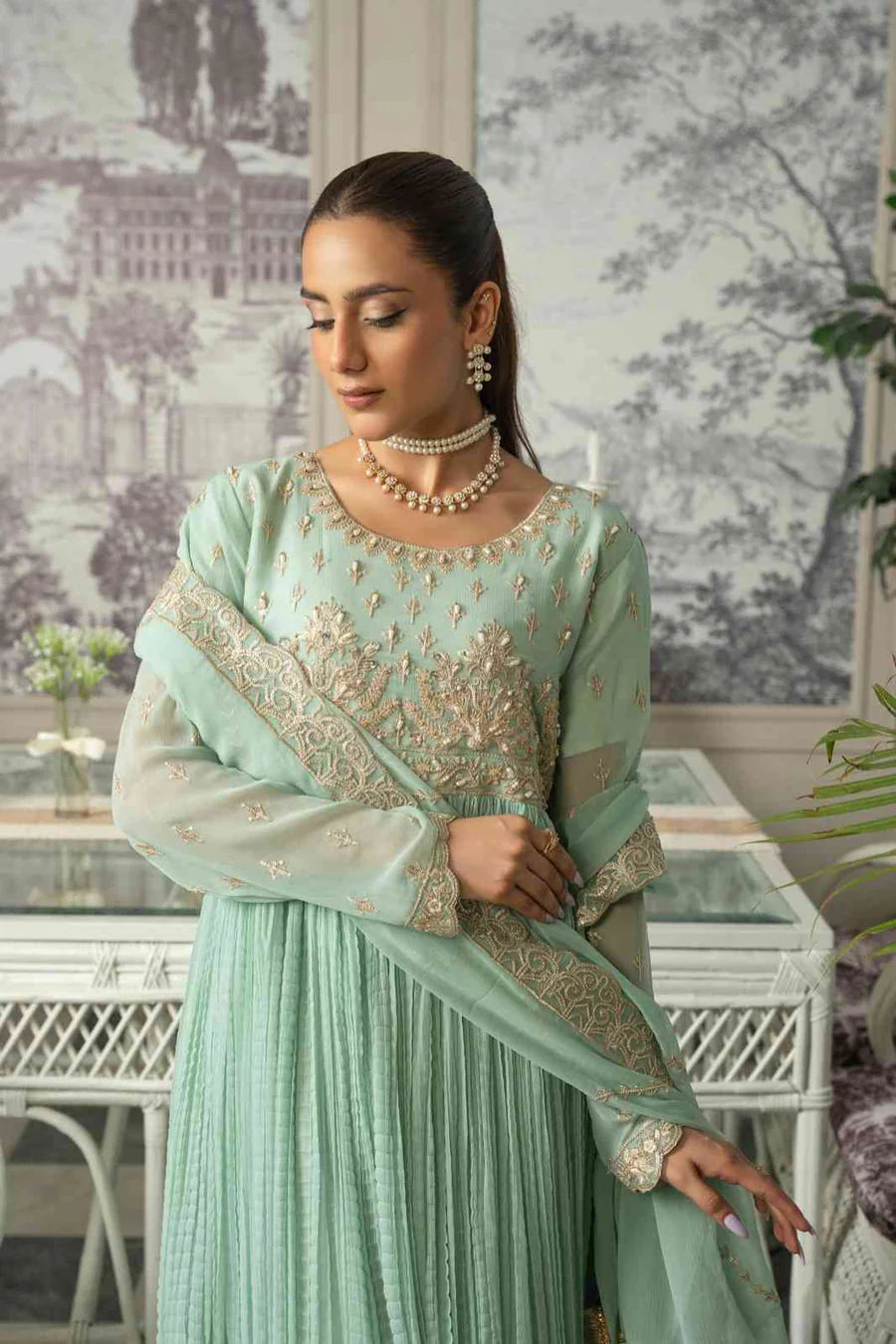 Woman in a light green traditional outfit with intricate patterns, standing indoors.