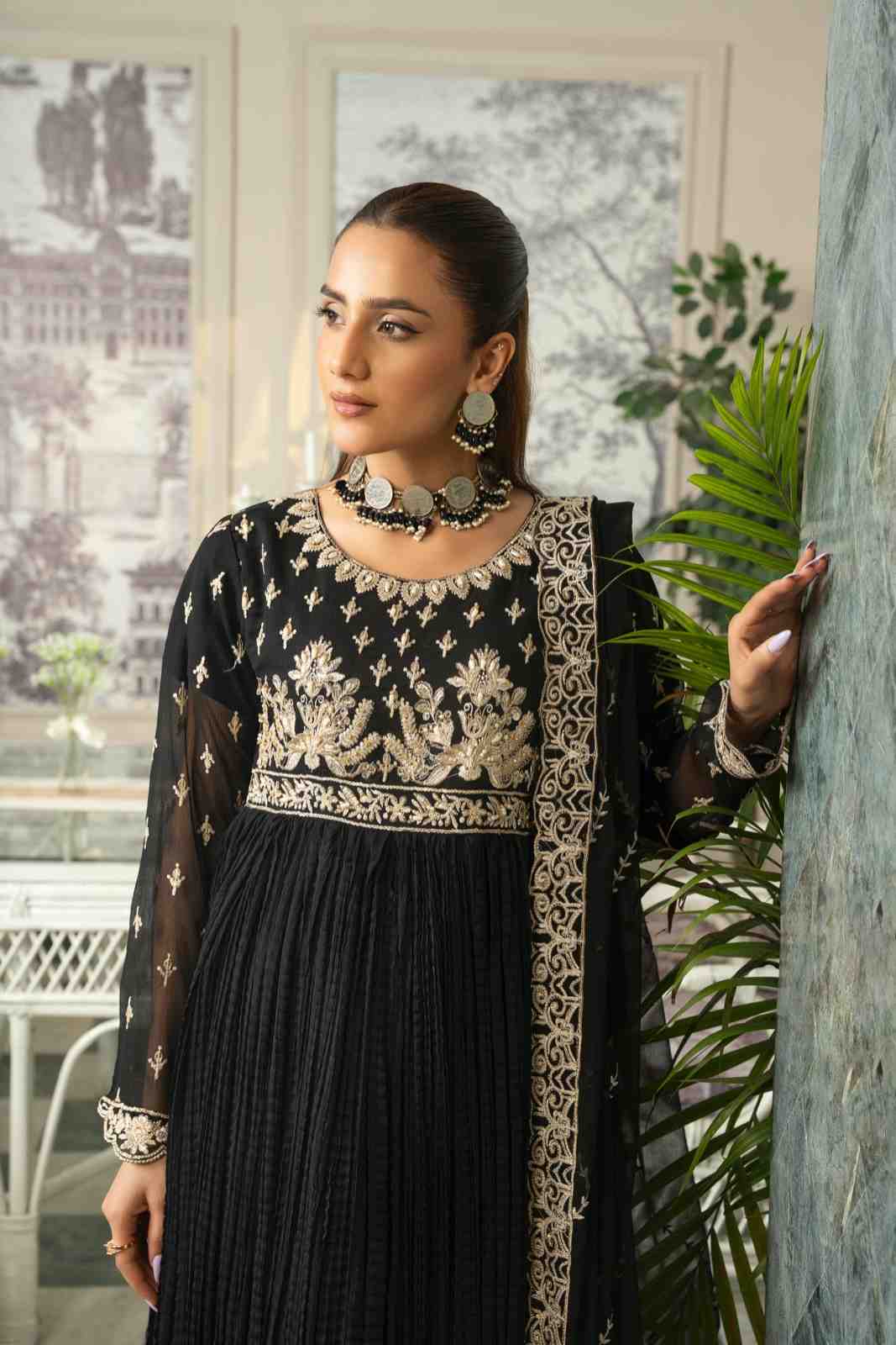 Woman wearing a black and gold embroidered outfit with a plant in the foreground 