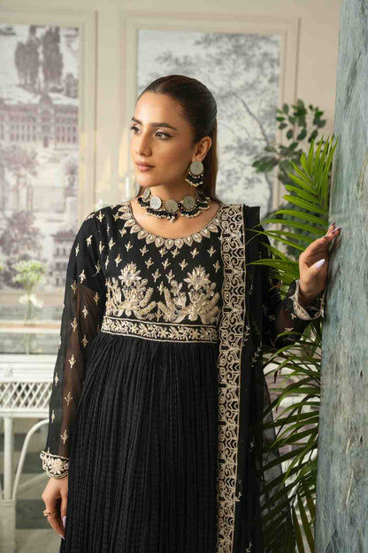 Woman wearing a black and gold embroidered outfit with a plant in the foreground 