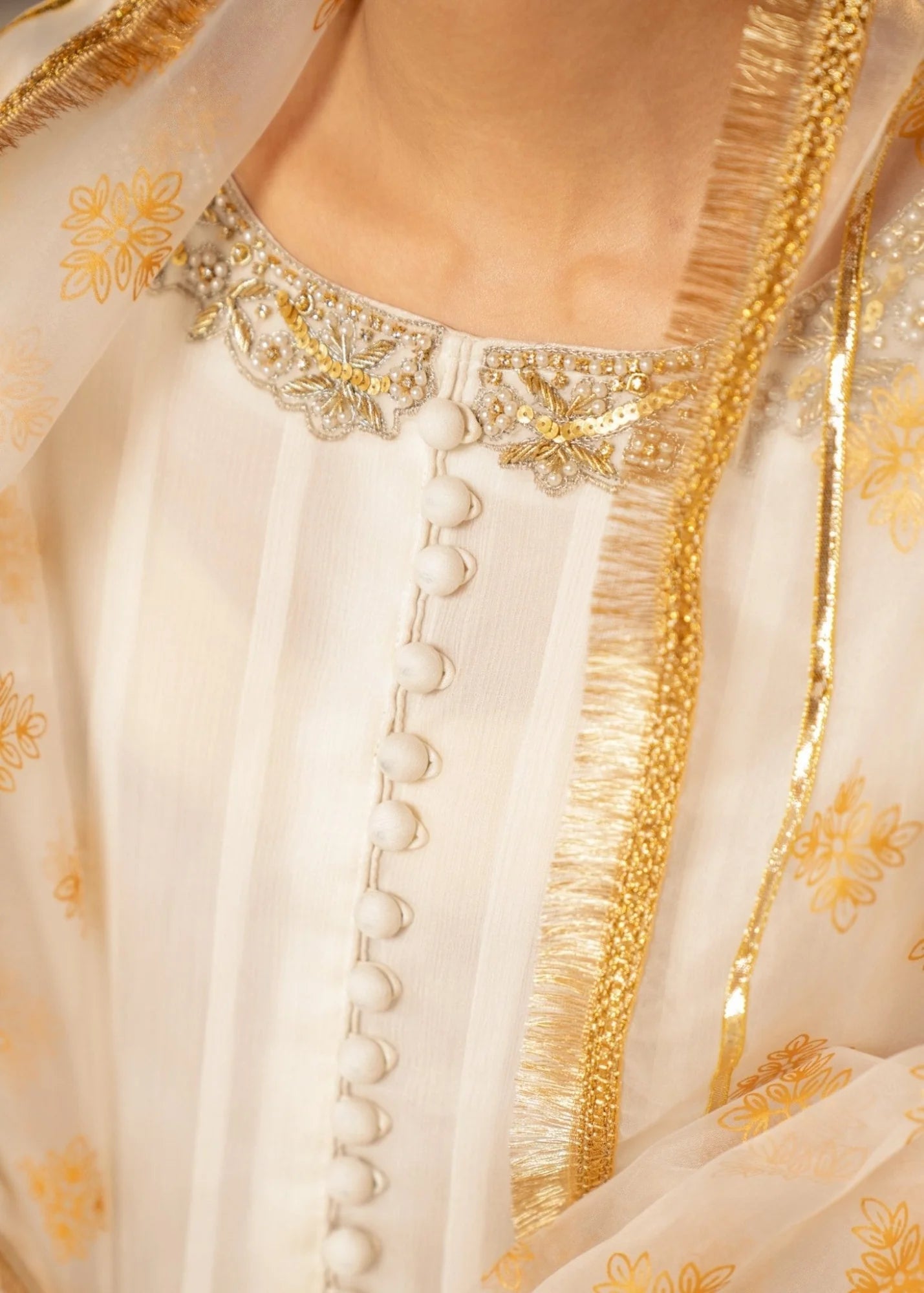 Close-up of a cream-colored garment with gold embroidery and embellishments.
