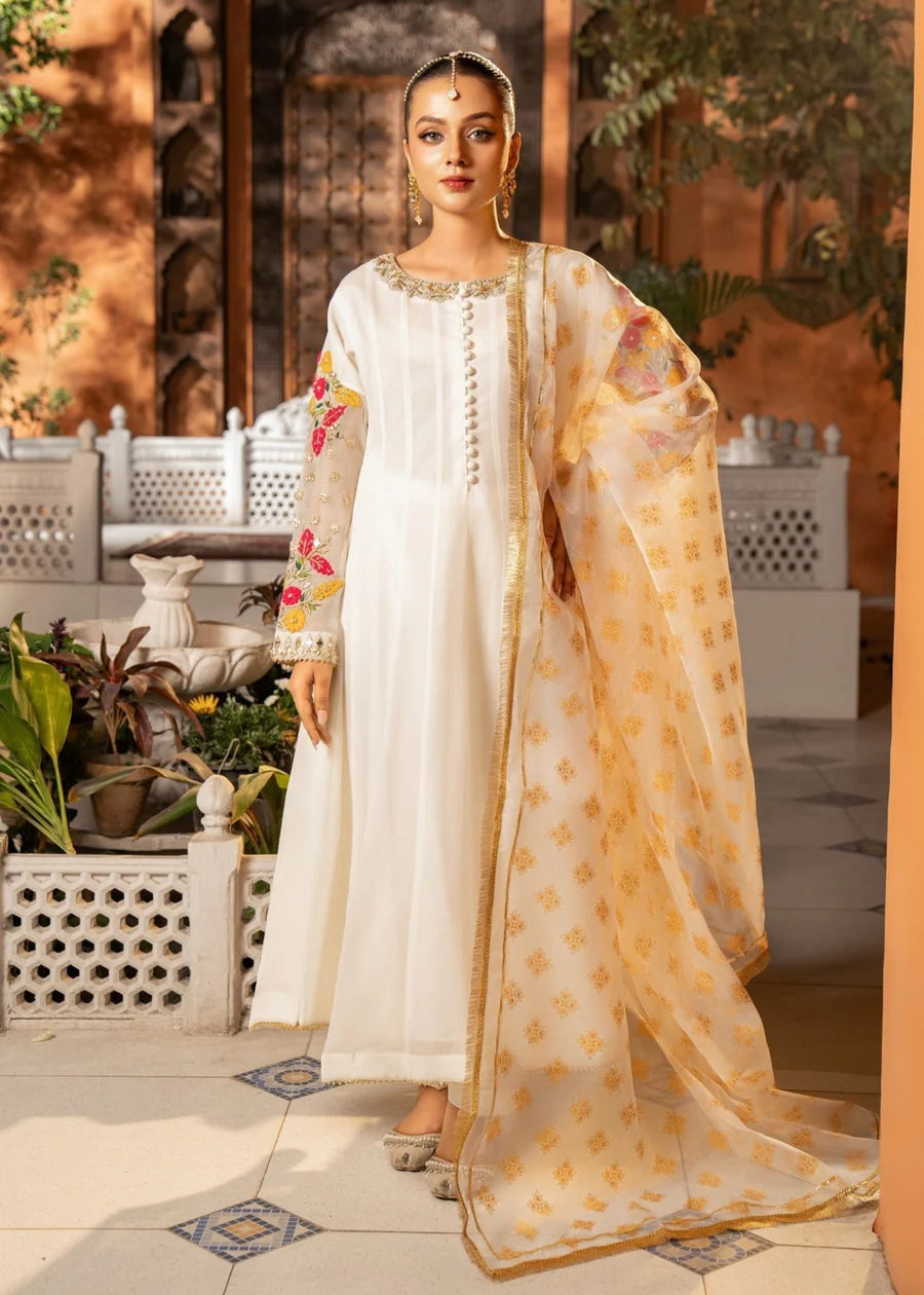 Woman in traditional white and gold outfit with floral patterns in an outdoor setting.