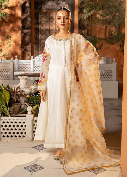 Woman in traditional white and gold outfit with floral patterns in an outdoor setting.